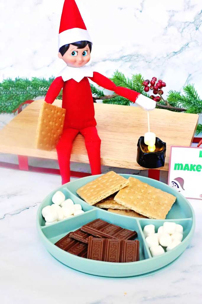 Elf on the Shelf Idea Elf Campfire  Cultivating Brilliant Minds an elf on the shelf roasting a marshmallow over a flameless candle next to ingredients for s'mores with a sign that reads "let's make s'mores!"